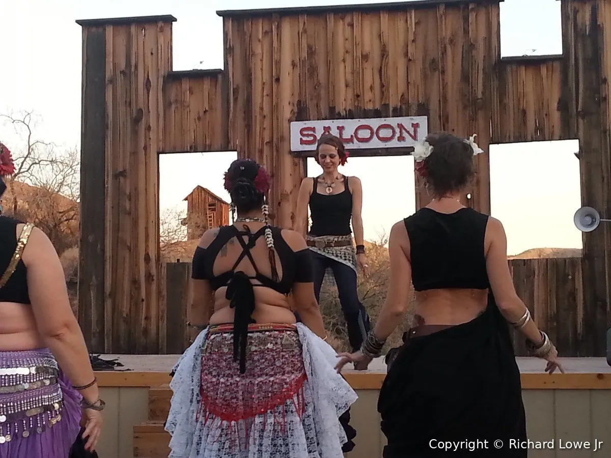 Belly dance instructor Heather Shoopman teaching a class of dancers from a stage in front of an old western saloon facade at a ghost town