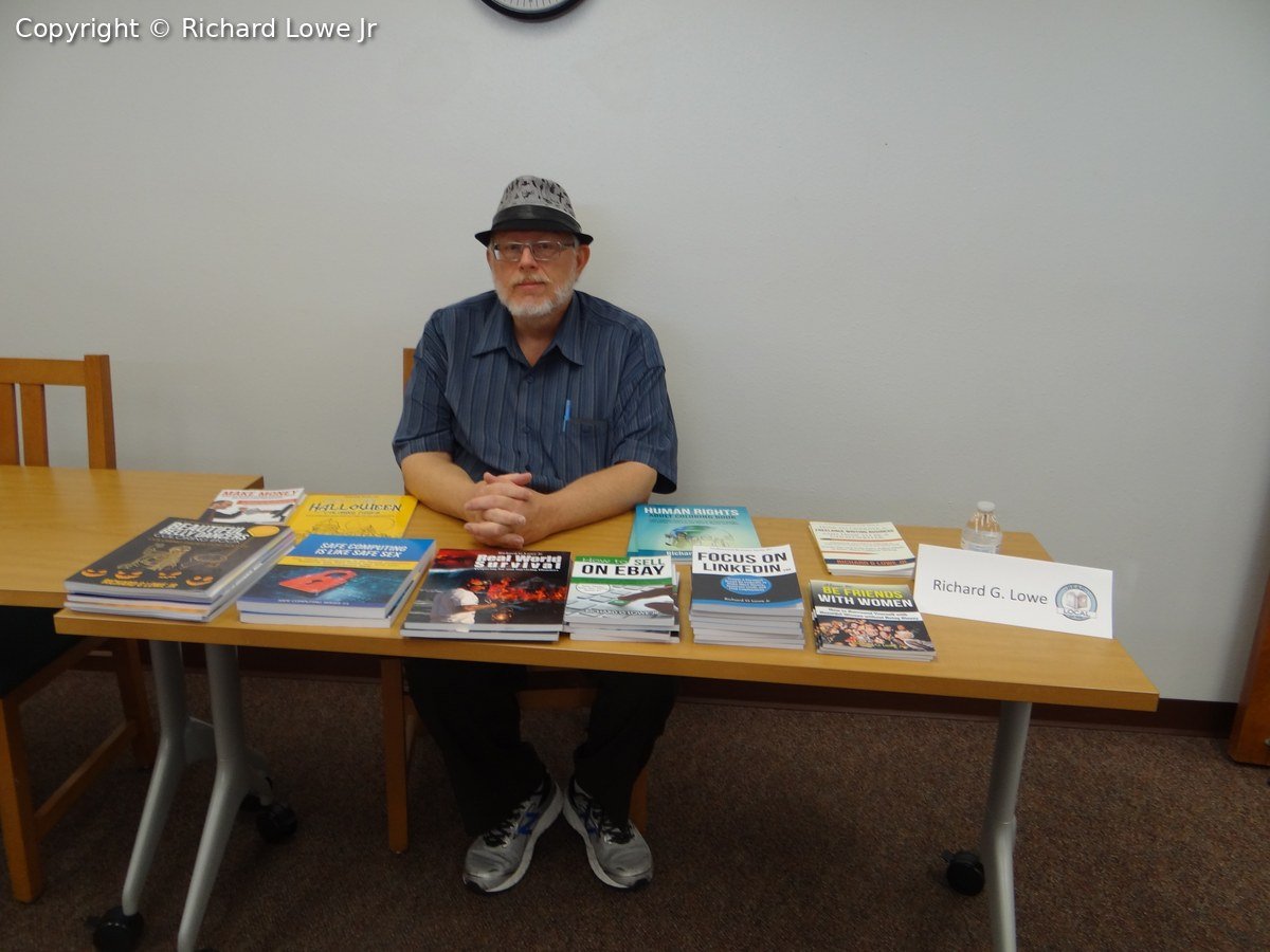 Richard Lowe seated behind a table of his books, including Real World Survival, Focus on LinkedIn and Safe Computing Is Like Safe Sex, at a local author event